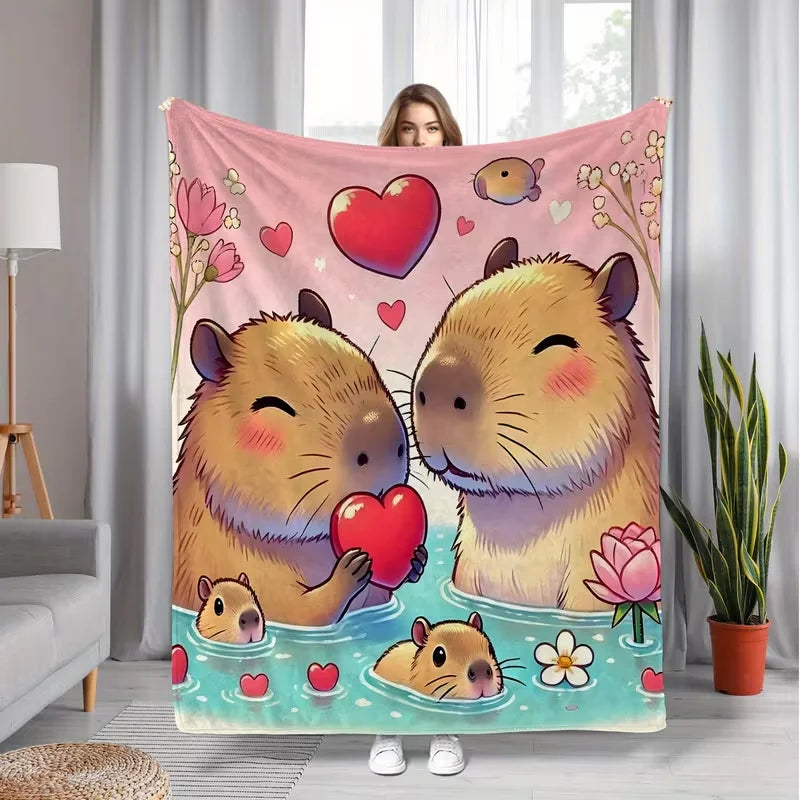A pink flannel throw blanket featuring a cartoon illustration of two cute, fluffy capybaras swimming in blue water.