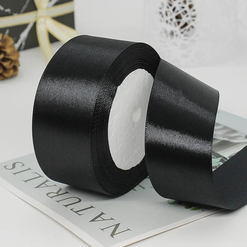 A roll of black satin ribbon used for gift wrapping or DIY crafts, shown on a white surface.