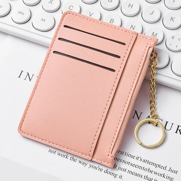 A pink leather slim zippered card wallet with three slots is shown next to a white laptop keyboard.
