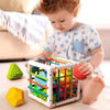 A toddler plays with a white plastic Montessori rainbow grasping ball that functions as a rattle, teether, and shape sorter.