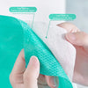 A hand is holding a teal disposable toilet seat cover, showing the layered structure of native wood pulp paper and waterproof