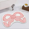 A pink, bow-shaped absorbent non-slip doormat with a decorative silver handle is shown on a white surface.