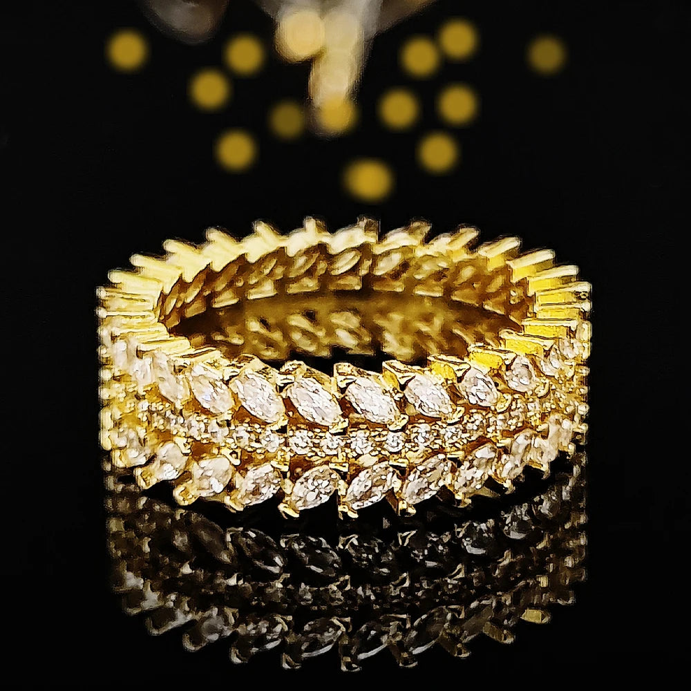 A close-up shot of a gold Marquise Zircon eternity band ring resting on a reflective black surface.