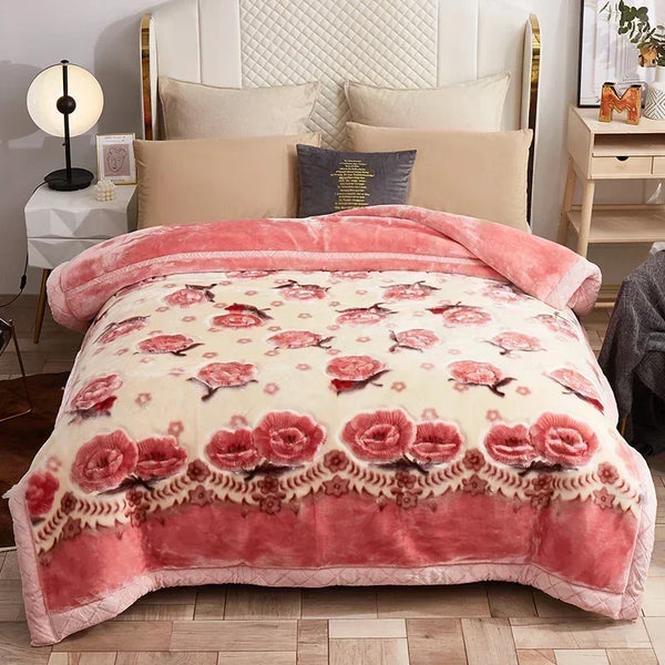 A pink and cream weighted plush blanket with floral embroidery is displayed on a bed.