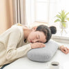 A person is resting their head on a gray memory foam travel neck pillow indoors near a window.