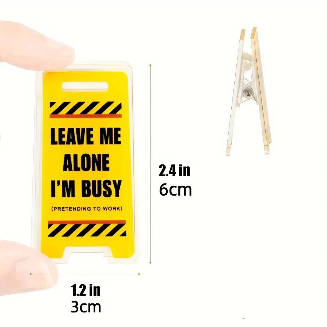 Yellow acrylic desk sign with black hazard stripes displaying the text Leave Me Alone I'm Busy