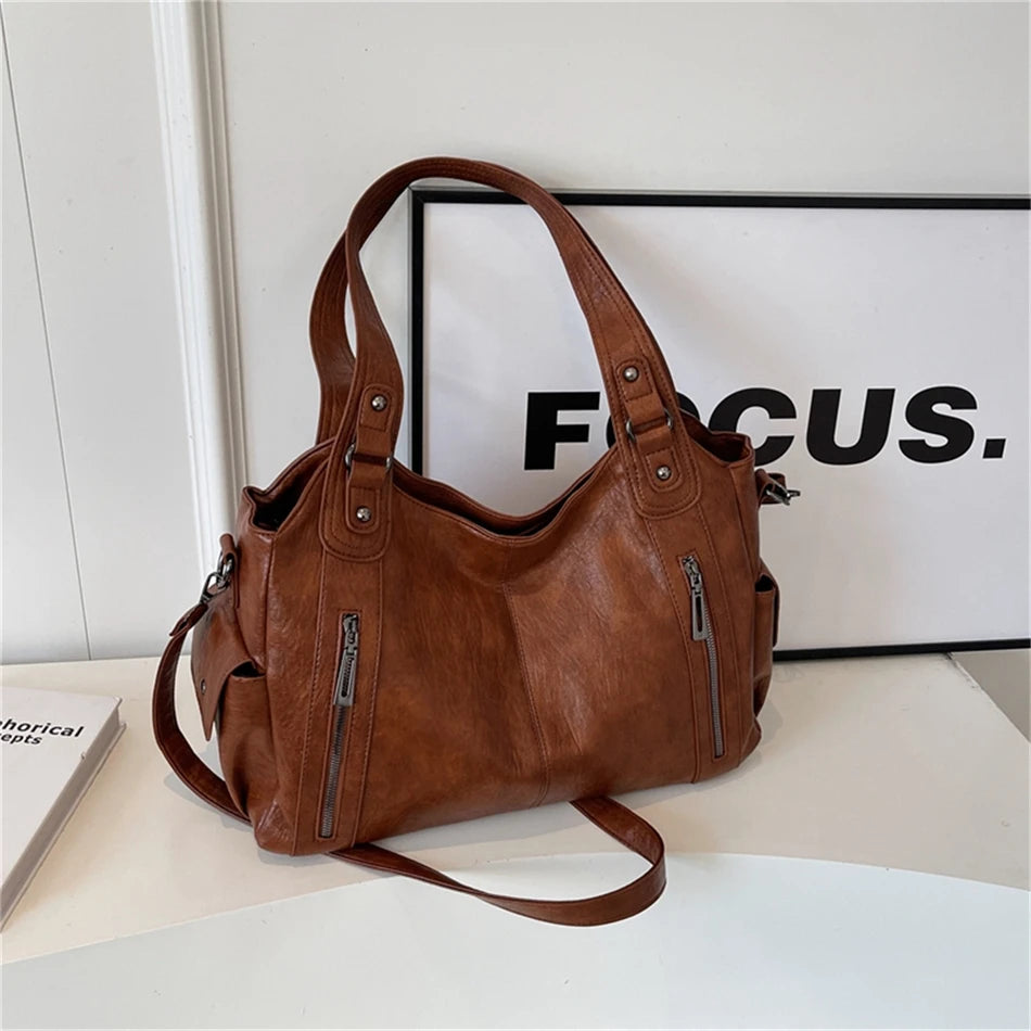 A brown vintage leather tote bag with multiple zippered pockets is displayed on a white surface.