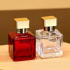 A clear glass perfume bottle with a gold sprayer cap and a red liquid, displayed on a wooden surface.