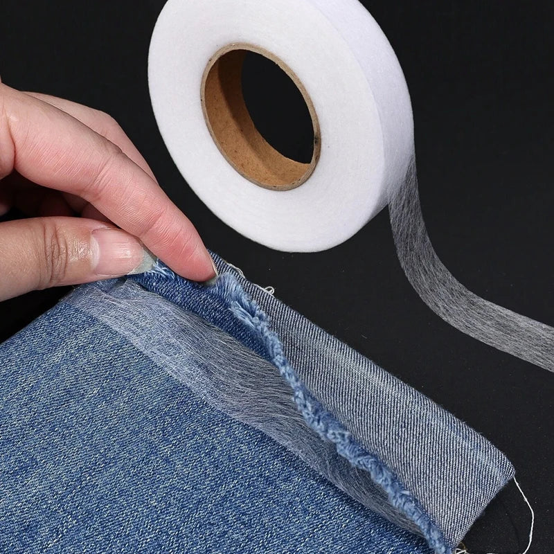 Eine Hand zieht ein Stück Denim-Stoff und zeigt den Rand, an dem strapazierfähiges doppelseitiges Zwischenfutterklebeband auf
