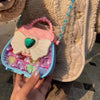 A hand holds a pink and white makeup toy set with a heart-shaped butterfly detail and a blue beaded strap.