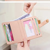 A light pink bi-fold credit card wallet with a leather strap and colorful cards is displayed in a hand.