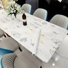 A white dining table set with gray chairs and a white tablecloth featuring a botanical pattern.