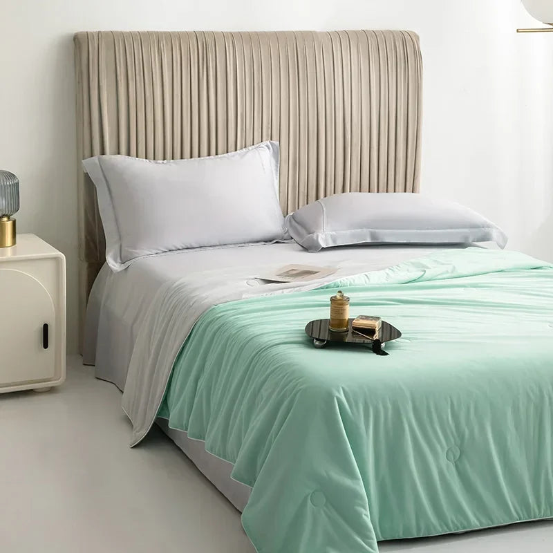 A light mint green cooling summer blanket is displayed on a bed with a neutral upholstered headboard.