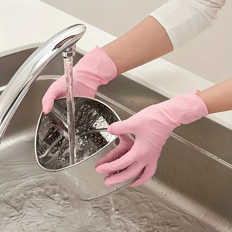 A hand wearing a pink disposable nitrile glove is using a faucet to rinse a metal cleaning tool in a stainless steel sink.