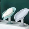 A leaf-shaped suction cup soap dish with a self-draining tray and white bar soap on a white sink.