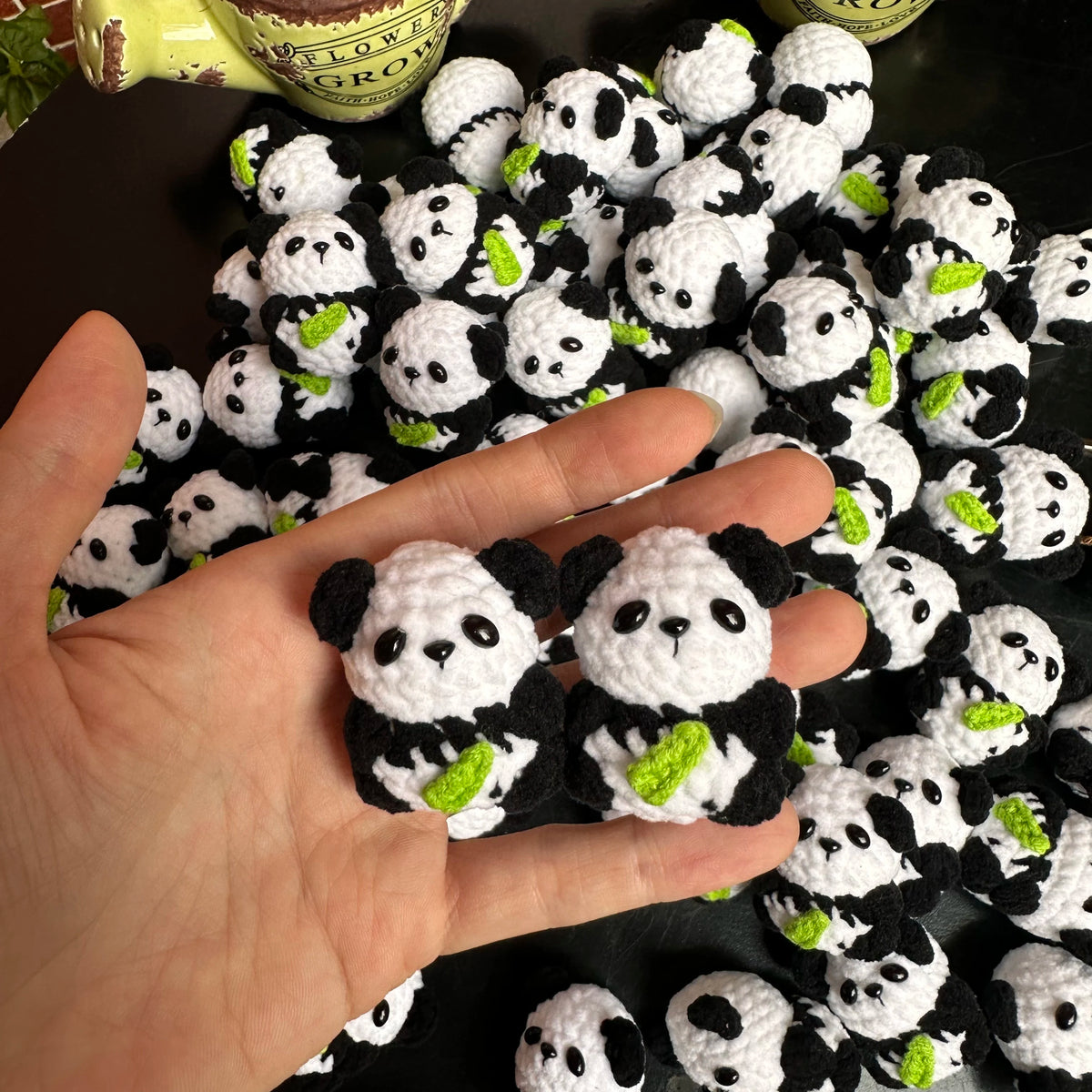 A hand holds a cluster of handmade crochet kitten keychains featuring cute panda and cartoon animal designs.