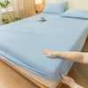 A light blue fitted sheet is laid out on a bed, showing its soft texture and elastic edge.