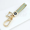 A gold-toned TPU key fob cover with a green stripe and a metal clasp, placed on a white surface.