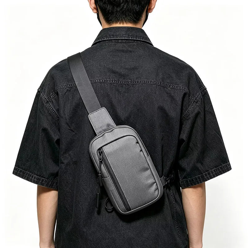 Eine Person in einem schwarzen Shirt von hinten, die eine graue Umhängetasche trägt.