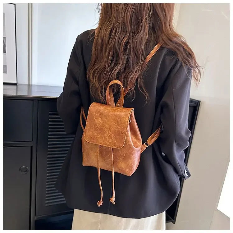 Une personne tient un mini sac à dos en cuir marron à cordon contre un fond clair.