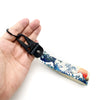 A hand holds a black keychain featuring a Kanagawa surf design on a light background.
