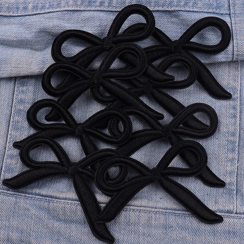 Black felt bow embroidery iron-on patches arranged on a denim fabric surface.