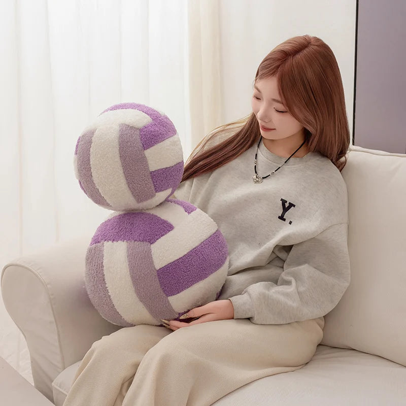 A young woman is sitting on a sofa holding a purple and white simulation volleyball plush toy pillow.