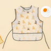 A light yellow waterproof baby feeding bib with a sleeveless design featuring small animal illustrations.