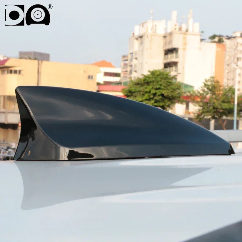 A black shark fin car antenna mounted on a white vehicle's roof.
