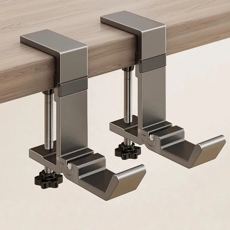 A close-up view of a metallic desk hook designed to hold bags and coats, mounted on a wooden surface.