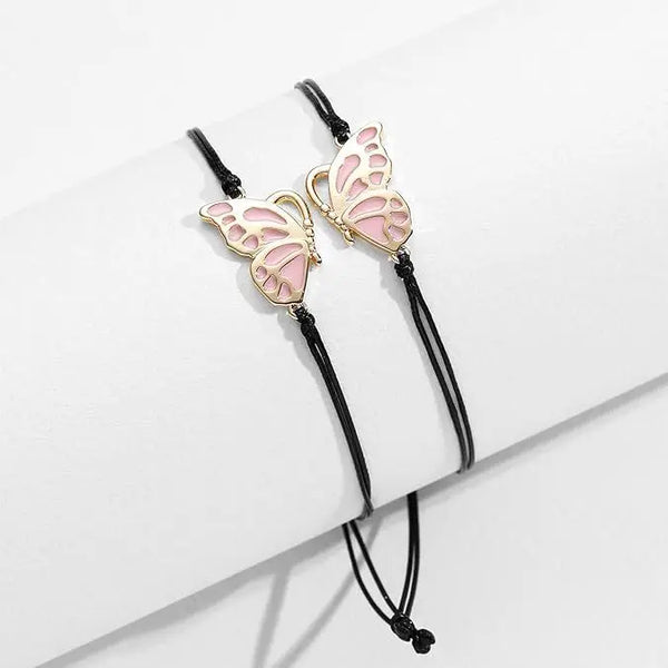Un par de pulseras de amistad con charms de mariposa rosa exhibidas sobre una superficie blanca.