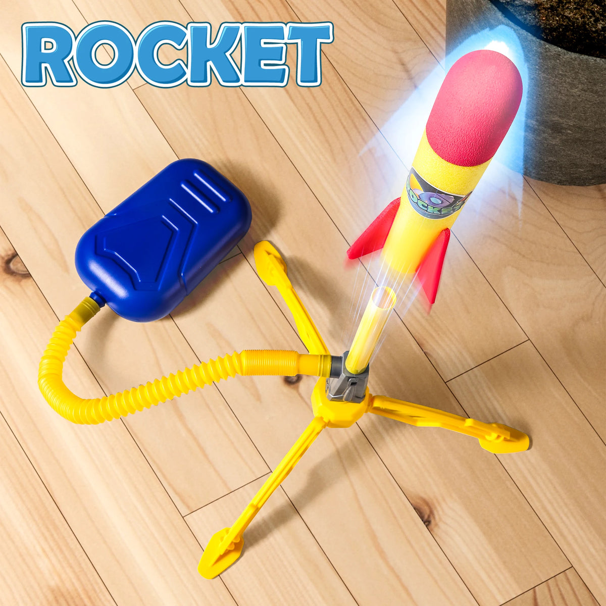 A yellow rocket launcher toy set with a pink and yellow nose cone and blue launching mechanism on a wooden floor.