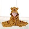 A baby wearing a cozy, tan hooded bathrobe towel with a cartoon lion design lying on a white surface.