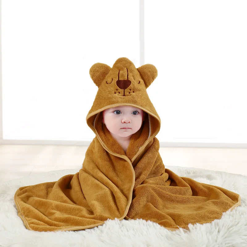 A baby wearing a cozy, tan hooded bathrobe towel with a cartoon lion design lying on a white surface.