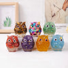 A collection of seven handcrafted crystal owl figurines in various colors and finishes displayed on a white surface.
