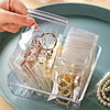A hand is holding a clear self-sealing jewelry storage box filled with various rings and bracelets.