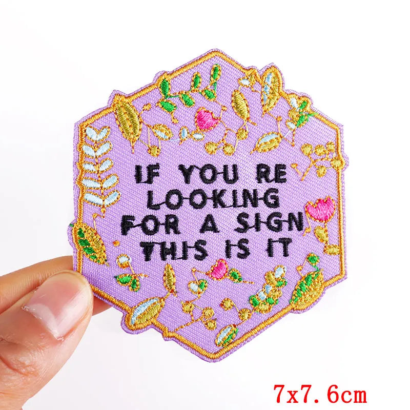 A hexagonal embroidered iron-on patch featuring pink and yellow floral designs with the text If you are looking for a sign th