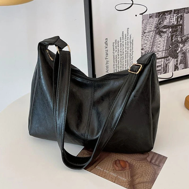 A black vintage-style PU leather tote bag is displayed on a white surface next to a framed print.