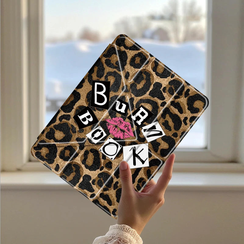A leopard print tri-fold iPad case with the word BURN on the front is held up against a window background.
