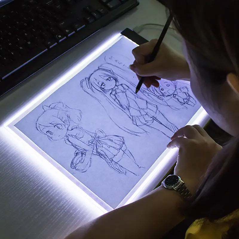 A person draws a figure on a transparent LED tracing light with a pencil, illuminated by the light.