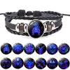 A black braided wrap bracelet featuring various zodiac sign charms with iridescent and glowing blue patterns.