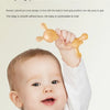 A baby is holding a yellow silicone teether shaped like a rabbit for grip practice.