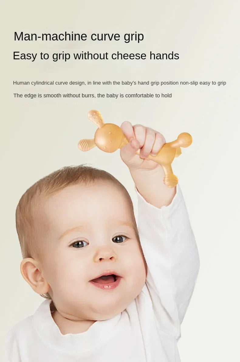 A baby is holding a yellow silicone teether shaped like a rabbit for grip practice.
