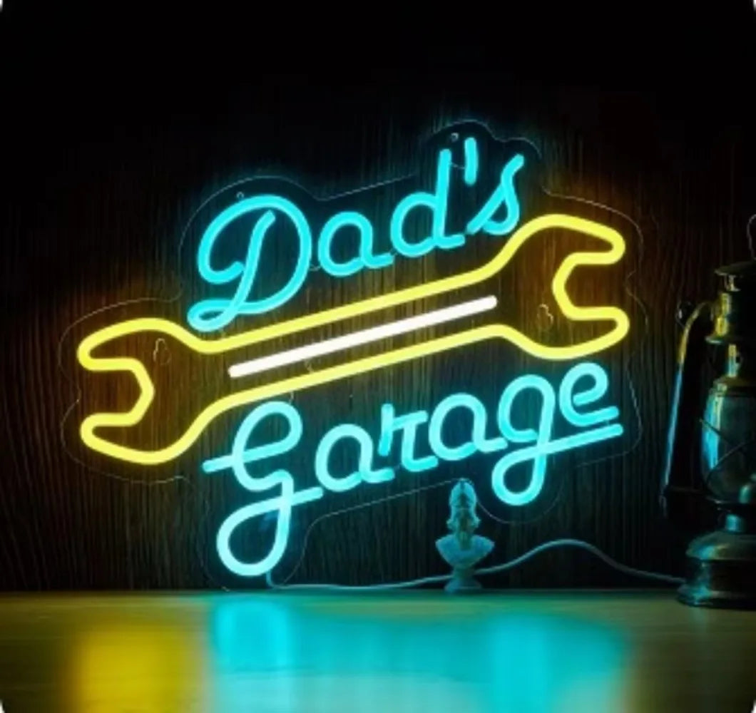Neon sign spelling out Dad's Garage in bright blue light on a dark wooden background.