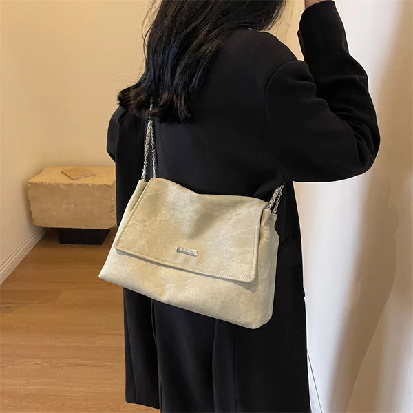 Eine Frau hält eine beige retro-Ketten-Leder-Schultertasche vor einer weißen Wand.