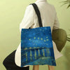 A canvas tote bag featuring a blue night sky with bright yellow stars and a reflection of water.