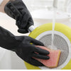 A hand wearing a black rubber cleaning glove is using it to pour water over a piece of food in a yellow container.
