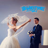 A bride in a white gown and veil is shown alongside a groom, with a neon sign reading The World Is Yours above them.