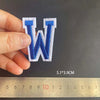 A hand holds a blue embroidered letter W patch, measuring 5.1 by 3.9 cm against a ruler.