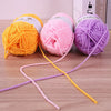 Three balls of premium acrylic yarn in yellow, pink, and purple lying on a wooden surface with loose strands.